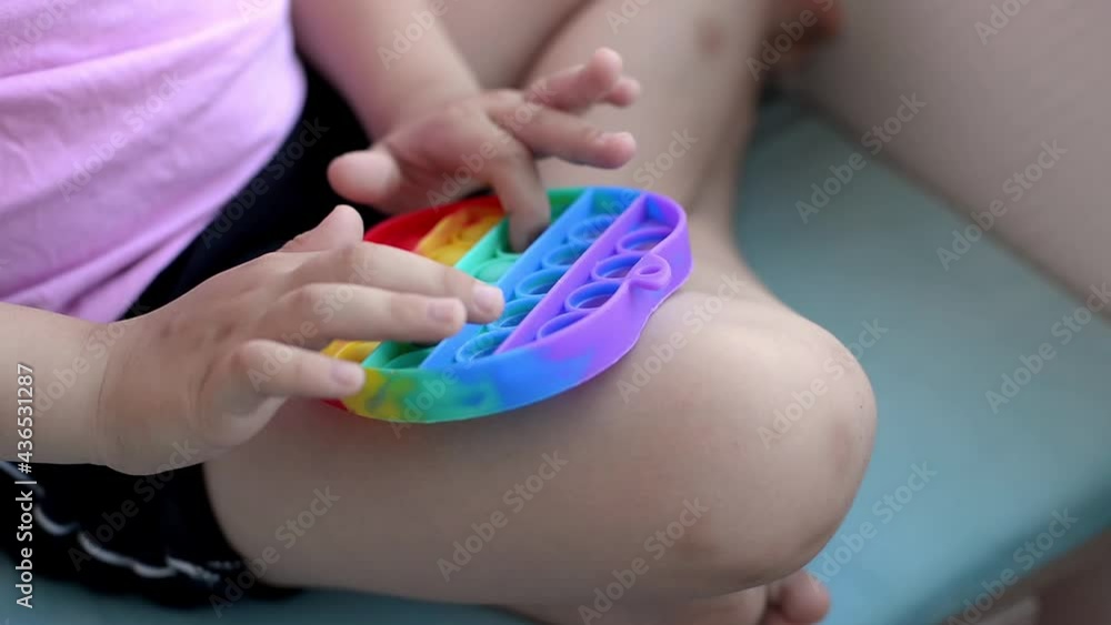 a girl in a pink t-shirt plays with a trendy toy pop it. colorful antistress sensory toy fidget push pop it in kid's hands, can be used for training with autistic people a girl in a pink t-shirt plays with a trendy toy pop it. colorful antistress sensory toy fidget push pop it in kid's hands, can be used for training with autistic people