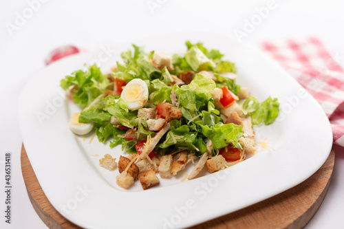 Caesar salad with chicken and eggs on a white plate close up