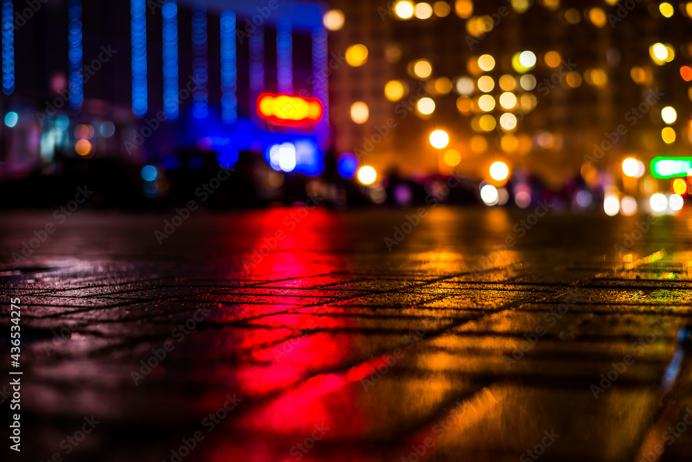Rainy night in the big city, light from the shop windows and the windows of the house is reflected in the asphalt. View from the sidewalk level paved with bricks Rainy night in the big city, light from the shop windows and the windows of the house is reflected in the asphalt. View from the sidewalk level paved with bricks