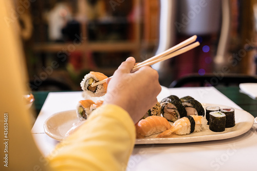 Sushi Japanese food close-up with woman hand in a restaurant. Lifestyle sashimi tasty seafood and rice rolls. Yellow color of the year photo