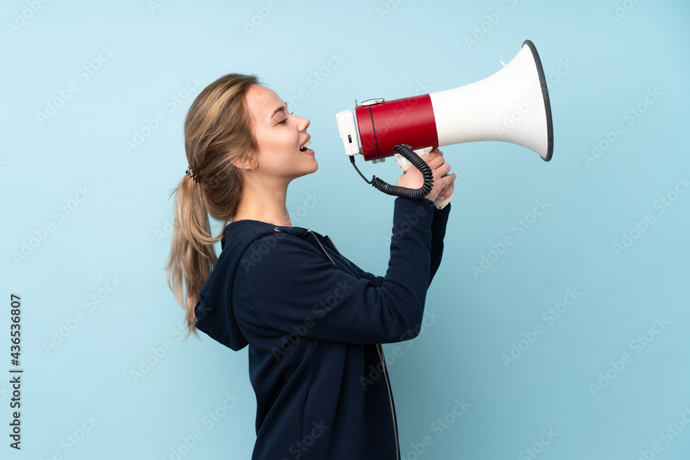 Teenager Russian girl holding mat isolated on blue background shouting through a megaphone Teenager Russian girl holding mat isolated on blue background shouting through a megaphone