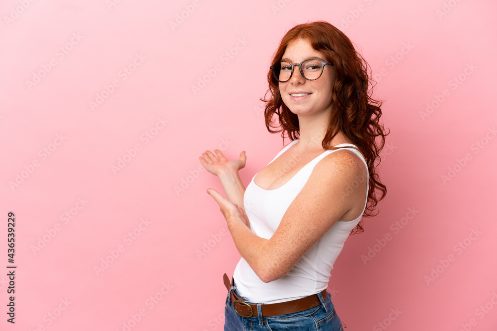 Teenager reddish woman isolated on pink background extending hands to the side for inviting to come Teenager reddish woman isolated on pink background extending hands to the side for inviting to come
