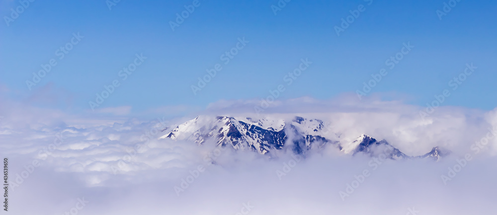 A picturesque, natural, minimalist landscape with a mountain peak above dense low clouds. The top of the mountain floats in thick clouds.