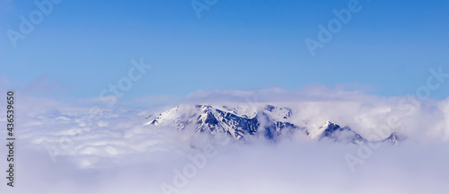 A picturesque, natural, minimalist landscape with a mountain peak above dense low clouds. The top of the mountain floats in thick clouds. © Евгения Якименко