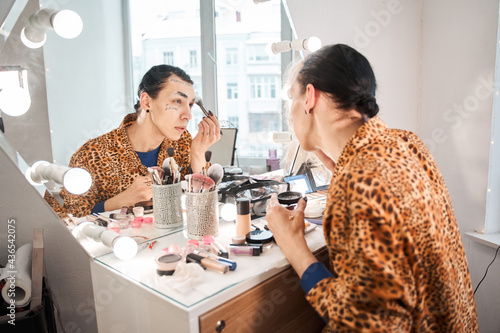 Fotografie Drag queen sitting in front of the mirror and puts on makeup