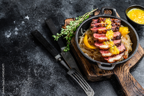 Grilled duck meat breast fillet steak with noodles and tangerines sauce. Black background. Top view. Copy space