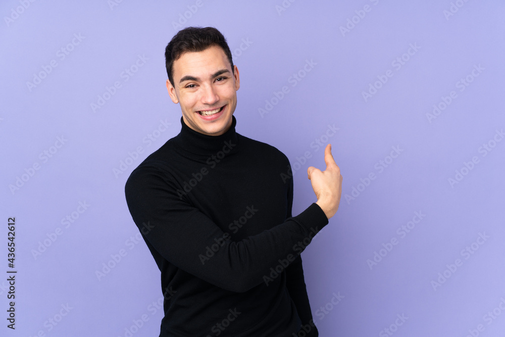 Young caucasian handsome man with turtleneck sweater isolated on purple background pointing back Young caucasian handsome man with turtleneck sweater isolated on purple background pointing back