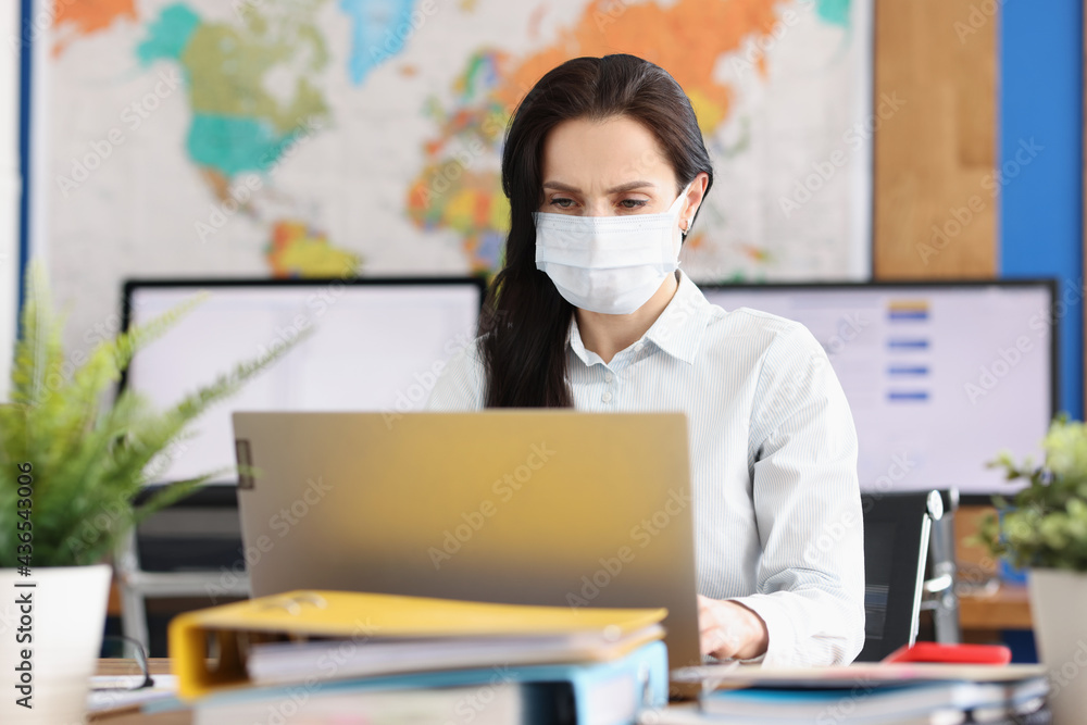 Woman in protective medical mask works at laptop Woman in protective medical mask works at laptop