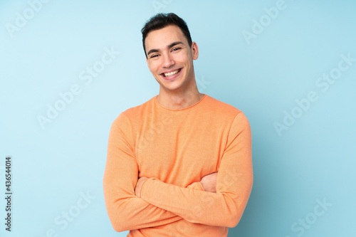 Young caucasian handsome man isolated on blue background keeping the arms crossed in frontal position