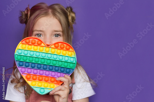 a baby girl holds a popular pop it toy in her hands. Sensory game for training with a neuropsychologist, for people with autism, for the development of fine motor skills photo