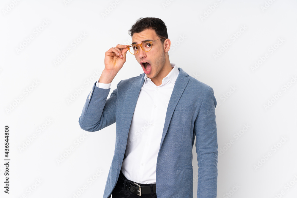 Young handsome businessman on isolated background with glasses and surprised Young handsome businessman on isolated background with glasses and surprised