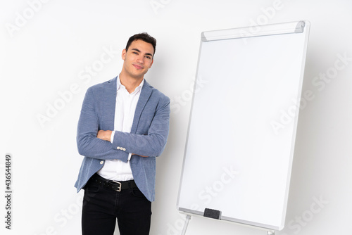 Young caucasian handsome man isolated on purple background giving a presentation on white board and smiling © luismolinero