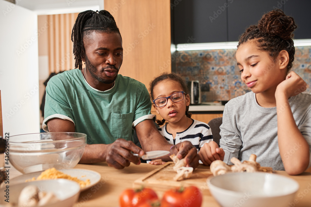 Father lovingly chopping mushrooms while preparing pizza with his daughters