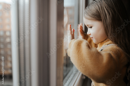 A little girl on the windowsill looks out the window from the apartment in a high-rise building photo