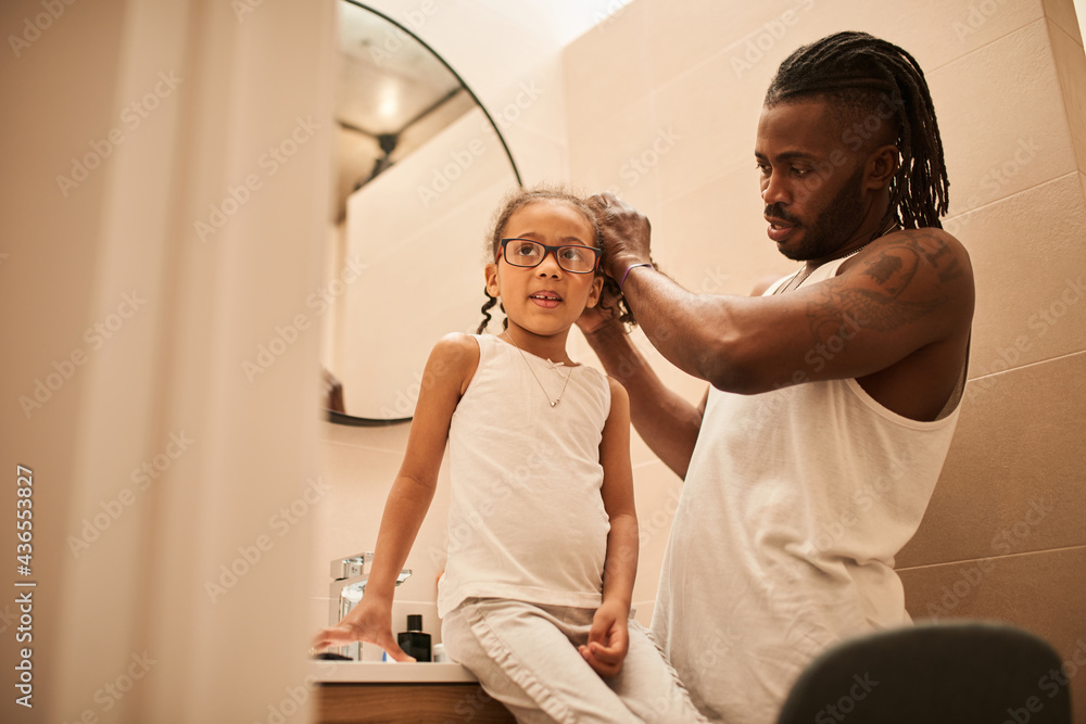 Multiracial man with dreadlocks doing hairstyle for his little daughter Multiracial man with dreadlocks doing hairstyle for his little daughter