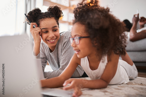 Girl laying at the floor with her little sister and smiling in front of the laptop