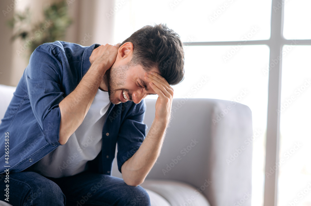Sick sad upset caucasian man in casual clothes sitting on sofa in living room bending over massaging his head and neck suffering from pain, migraine, closing his eyes, needs treatment and rest Sick sad upset caucasian man in casual clothes sitting on sofa in living room bending over massaging his head and neck suffering from pain, migraine, closing his eyes, needs treatment and rest