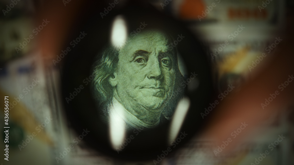 Person examine and controlling with magnifying glass front side of hundred dollar banknotes , concept of counterfeit money and finance