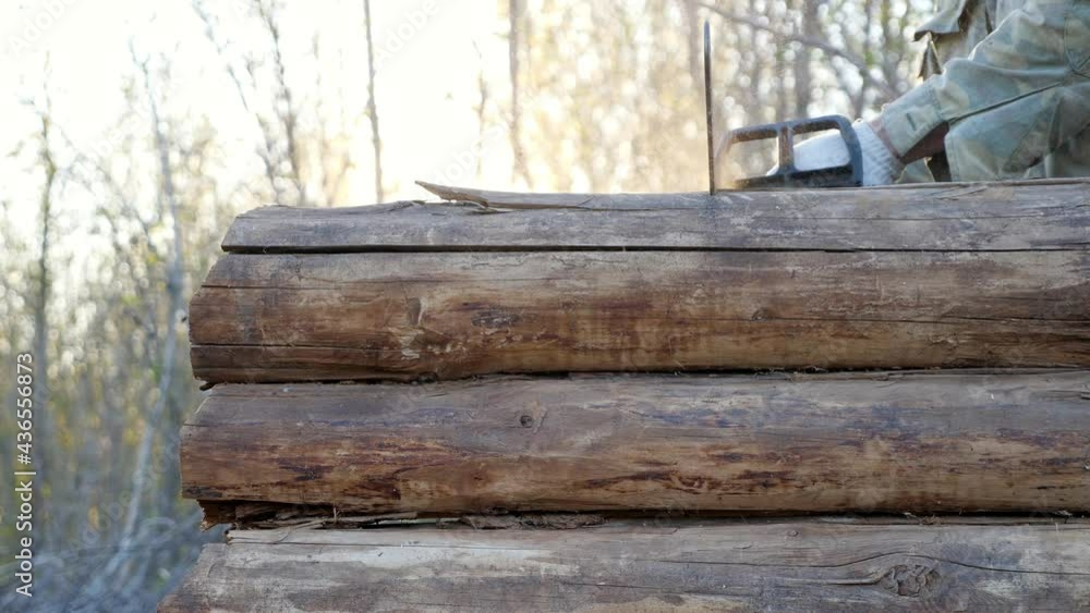 Unrecognizable man cuts a rotten wooden blockhouse with a chainsaw, sunlight. Unrecognizable man cuts a rotten wooden blockhouse with a chainsaw, sunlight.