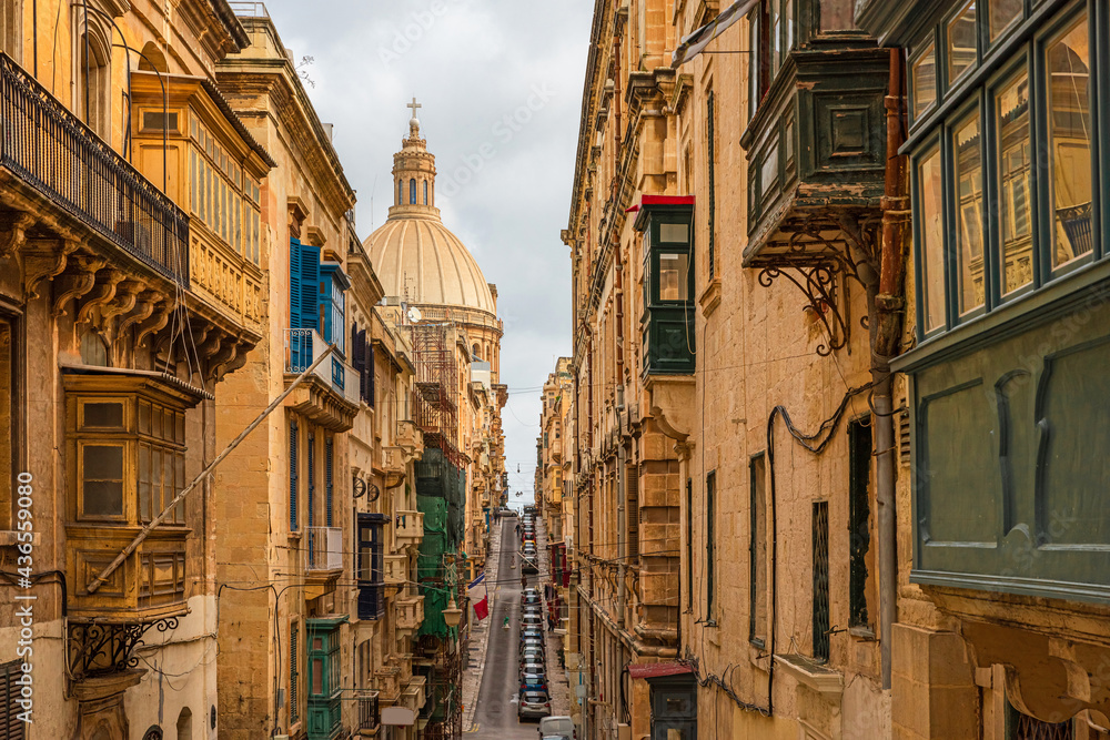 Typical narrow street of Valletta with Cathedral dome, yellow buildings and colorful balconies, Malta, Europe