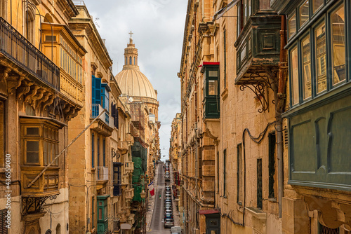 Typical narrow street of Valletta with Cathedral dome, yellow buildings and colorful balconies, Malta, Europe