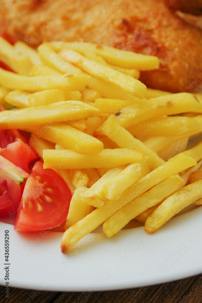 Traditional english dish with battered white cod, french fries and fresh vegetable served on a white plate. Close up. Vertical image Traditional english dish with battered white cod, french fries and fresh vegetable served on a white plate. Close up. Vertical image