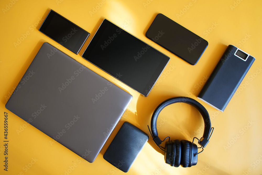 Obraz premium External charger - powerbank, laptop, external hard drive, smartphones and tablet lie on a bright yellow background. Concept of wireless gadgets and kit for geek or modern traveler