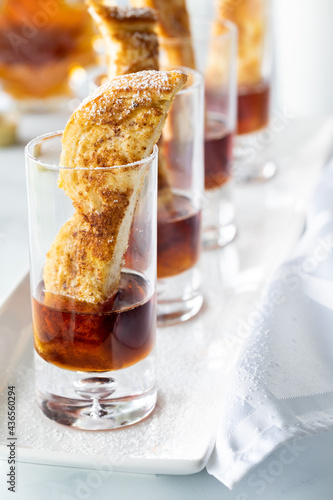 A row of french toast finger food appetizers in shot glasses with maple syrup.