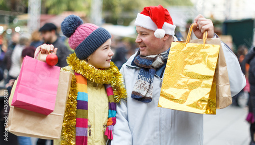 Portrait of smiling teen girl with her loving father holding shopping bags with purchases on street Christmas market