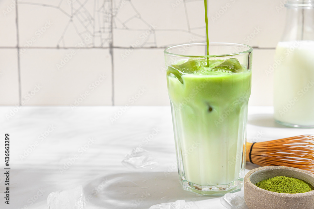 Iced green matcha latte and pouring tea in glass on white background with hard shadows. Cold summer drink Iced green matcha latte and pouring tea in glass on white background with hard shadows. Cold summer drink