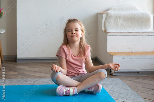 Portrait of little girl doing yoga sitting in lotus position on yoga mat