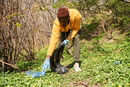 Multiracial volunteer helping to pick up waste by garbage bags