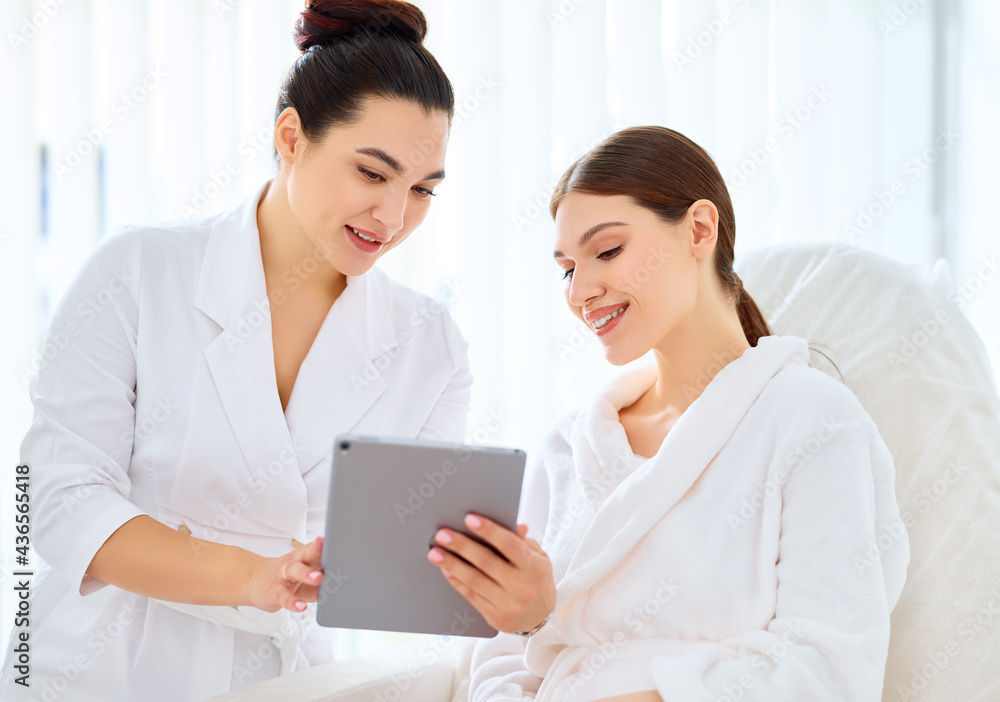 Cosmetologist and woman using tablet in clinic Cosmetologist and woman using tablet in clinic