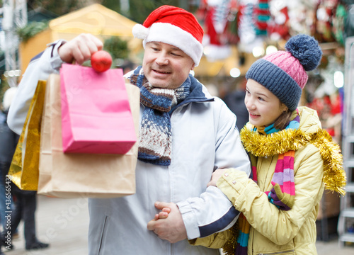 Portrait of smiling teen girl with her loving father holding shopping bags with purchases on street Christmas market