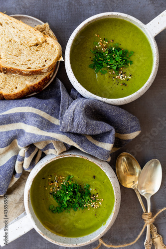 Green soup with toppings in white ceramic, napkins, spoon, bread slices on a gray surface photo