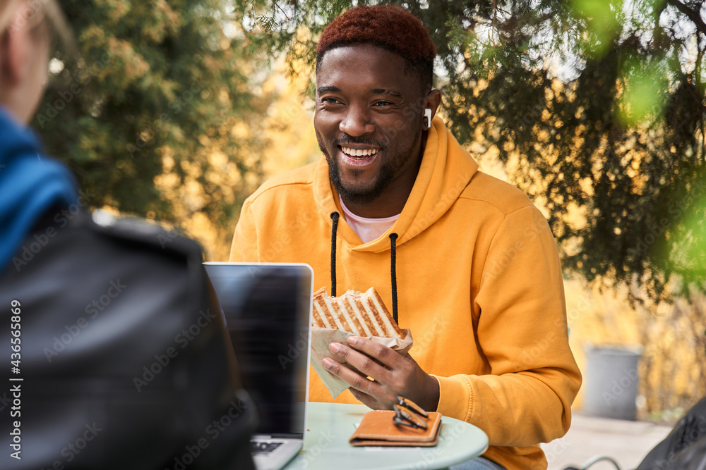 Man chatting during coffee break with his friend and eating sandwich Man chatting during coffee break with his friend and eating sandwich