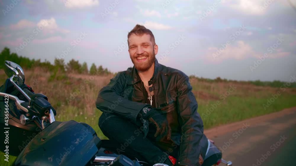 Young man sitting on motorcycle on the road at sunset, slow motion Young man sitting on motorcycle on the road at sunset, slow motion