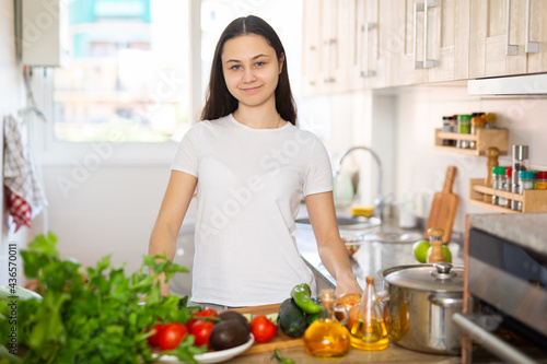 Positive young woman standing at kitchen interior  posing on camera