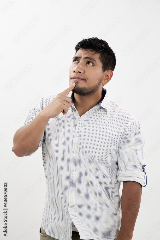 Hombre latino pensando mientras mira hacia arriba con su dedo en el mentón Hombre latino pensando mientras mira hacia arriba con su dedo en el mentón
