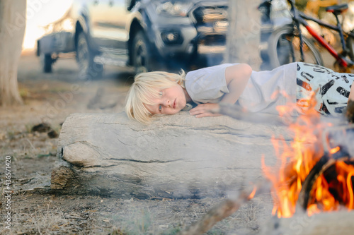 Little boy lying on log in front of campfire in the Australian bush