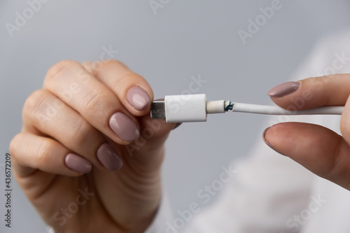 Close-up woman holding torn phone charger type-c wire.