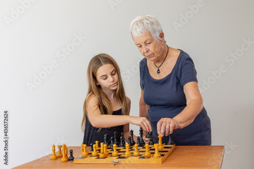 Menina com atenção na organização de peças num tabuleiro de xadrez com avó photo