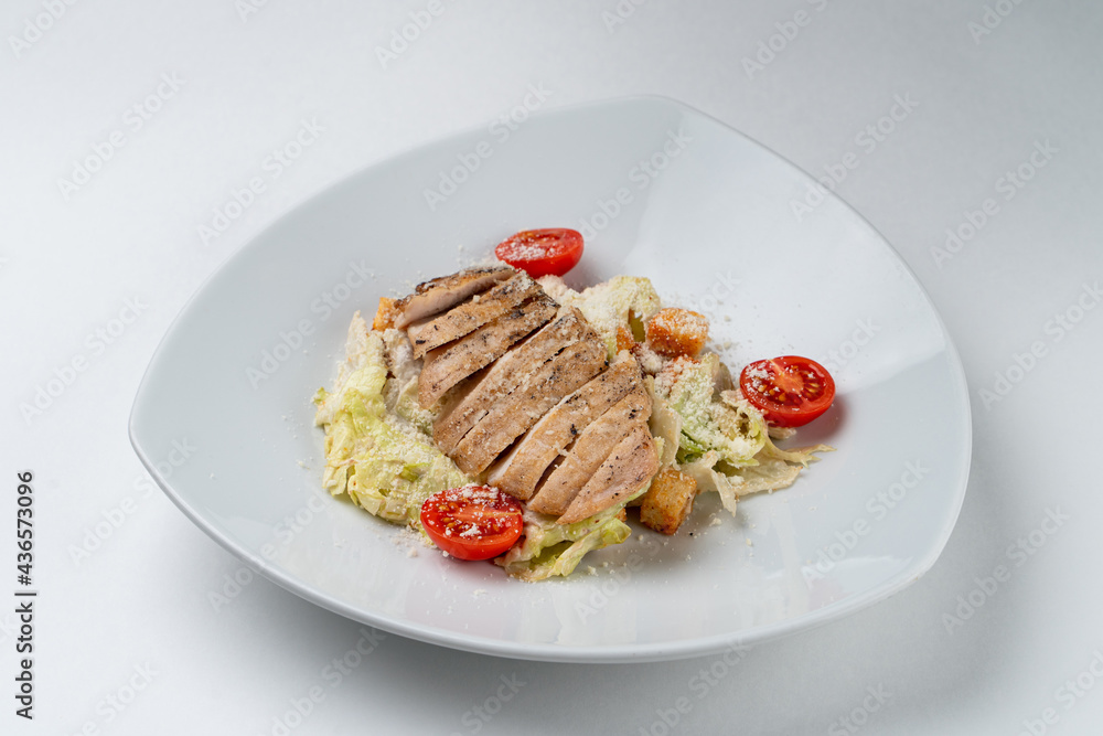 Classic caesar salad with crunchy lettuce and a whole grilled chicken breast, isolated on white background in a studio