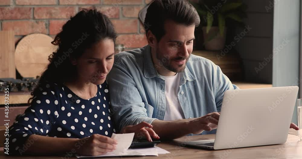 Happy young loving family couple sitting at table, calculating domestic utility bills, paying taxes online, managing monthly budget, feeling satisfied with enough money, financial independence concept Happy young loving family couple sitting at table, calculating domestic utility bills, paying taxes online, managing monthly budget, feeling satisfied with enough money, financial independence concept