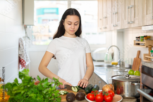Portrait of young positive woman cutting vegetables  preparing healthy vegetarian dinner at home