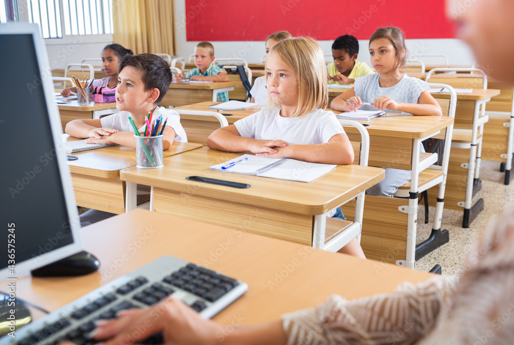 Fototapeta premium Group of focused pupils sitting at classroom working at class with teacher, looking at board