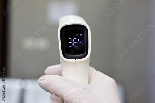 Non contact infrared forehead digital thermometer gun held by a medical personnel checking body temperature for virus symptoms on a defocused background - epidemic coronavirus outbreak concept. photo