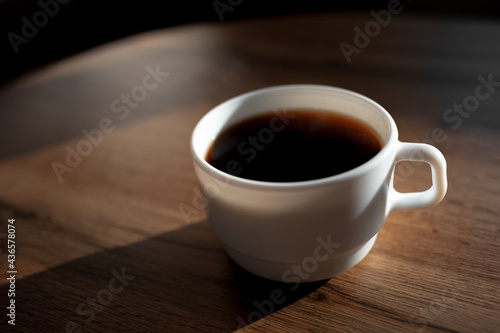 Close-up of white ceramic cup of coffee on wooden table.