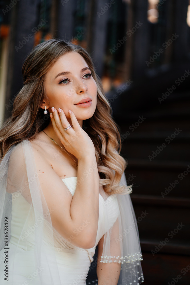 Naklejka premium beautiful and gentle bride sits on a dark wooden staircase. 