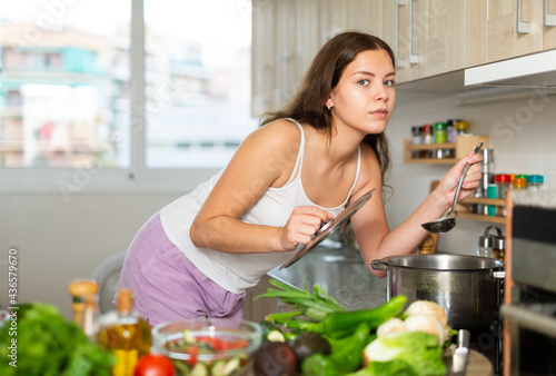 Young attractive housewife cooking soup in kitchen  holding spoon in her hand